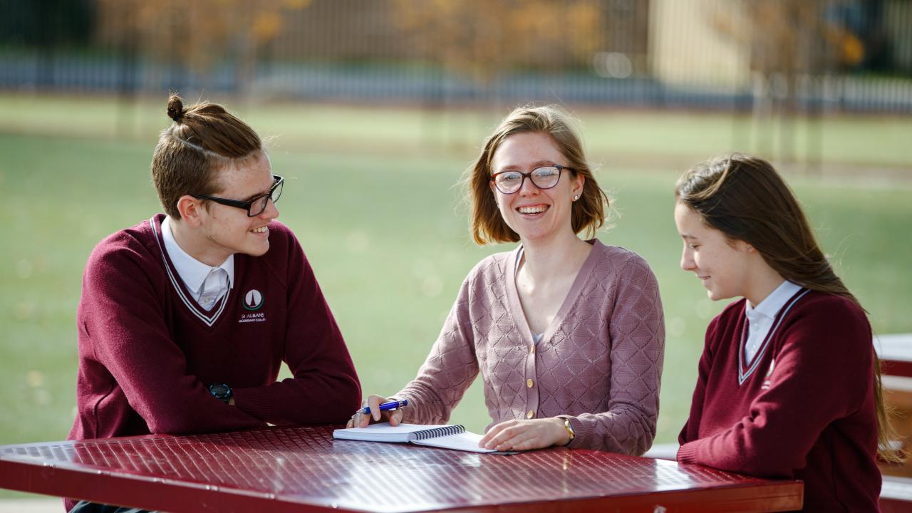 Female teacher sitting with high school students outdoors