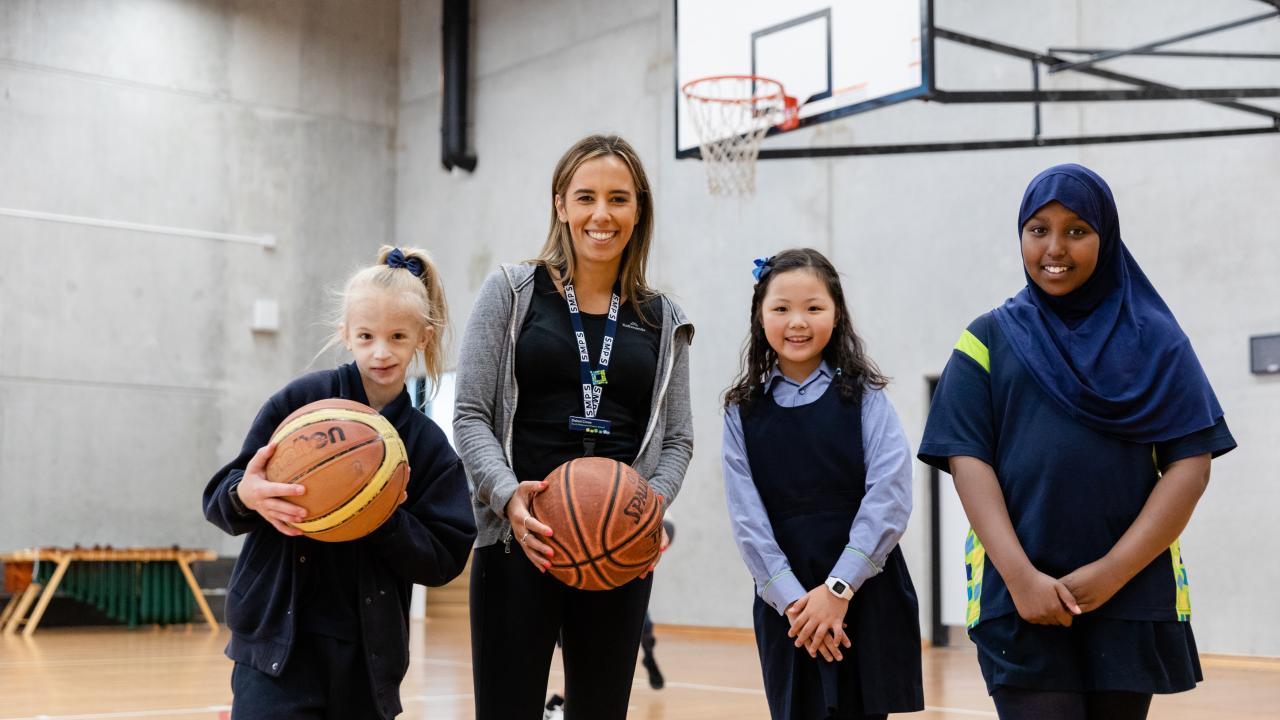 Teacher with primary school students holding basketballs inside school gym building